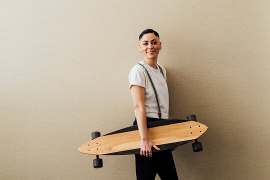 Young female entrepreneur holding skateboard while leaning on wall