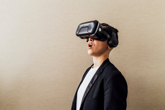 Businesswoman standing with mouth open while using virtual reality headset by wall in office
