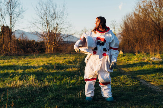 Thoughtful female explorer wearing space suit standing on grass land