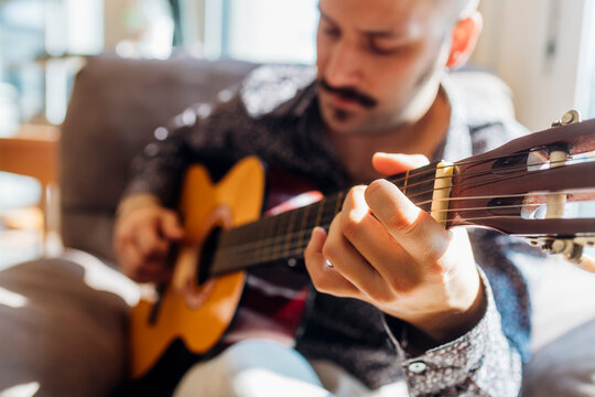 Young male guitarist playing guitar at home