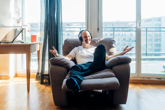 Smiling Man Wearing Headphones Gesturing While Sitting On Reclining Chair In Living Room