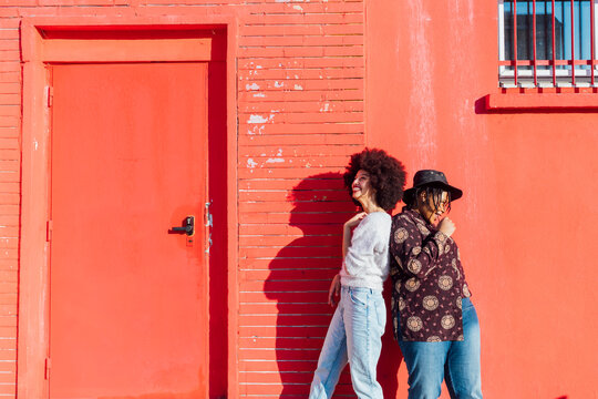 Smiling female friends standing back to back by red building