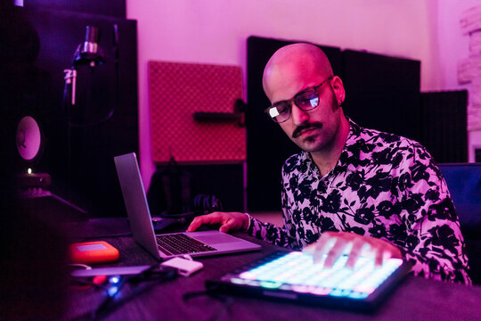 Male composer wearing eyeglasses touching digital tablet while composing music at studio