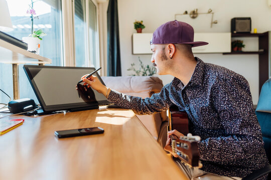 Young male composer with guitar using graphics tablet at home - Powered by Adobe