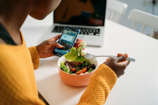 Young woman having healthy breakfast while using smart phone at home