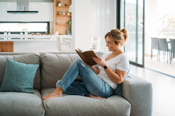 Female freelancer sitting on sofa while reading book at home