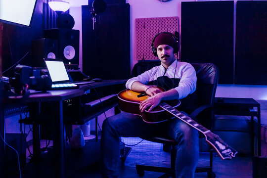 Male guitarist with guitar sitting at home recording studio