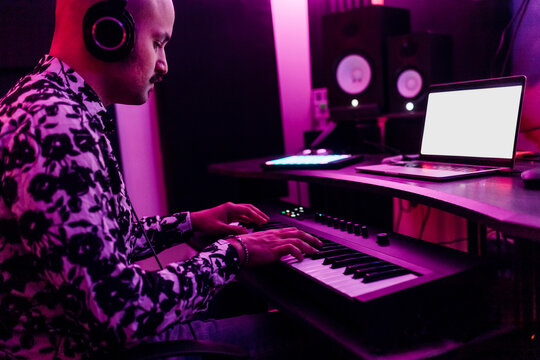 Young man wearing headphones playing piano while composing music at studio