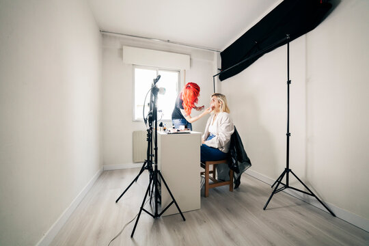 Female make-up artist applying face powder on model while blogging at studio