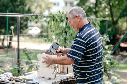 Active senior man with woodworking tool doing carpentry in backyard