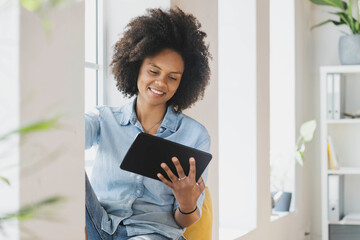 Smiling woman using digital tablet while sitting at window