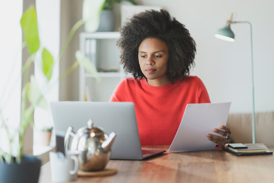 Curly hair woman with paper working on laptop at home