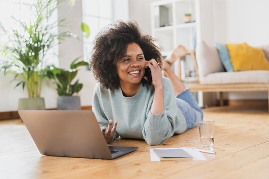 Smiling Young Woman Talking On Mobile Phone While Lying By Laptop At Home