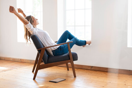 Woman Stretching Arms While Sitting On Chair In Front Of Window