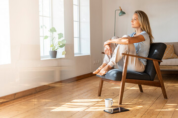 Woman day dreaming while sitting on chair at home