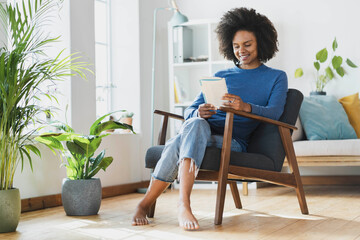 Smiling woman reading book while sitting on armchair at home