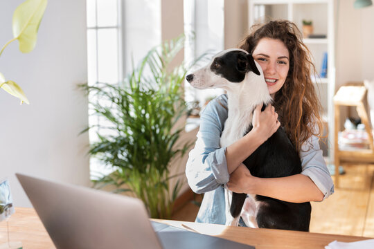 Happy businesswoman cuddling dog at desk in home office
