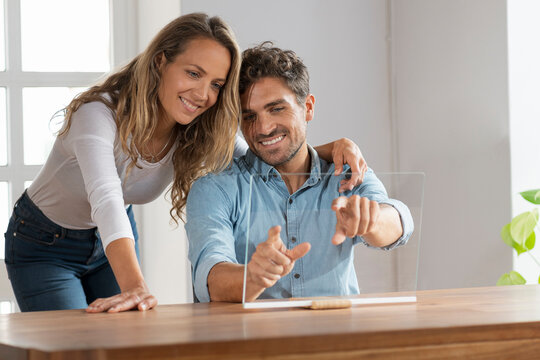 Beautiful woman embracing boyfriend touching transparent screen at home