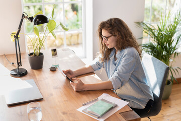 Young businesswoman with eyeglasses looking at digital tablet in home office