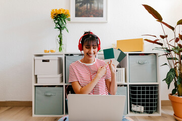 Smiling woman holding color swatch while attending video call on laptop