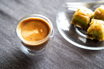 Close up transparent coffee cup on table with sweet dessert in the background.