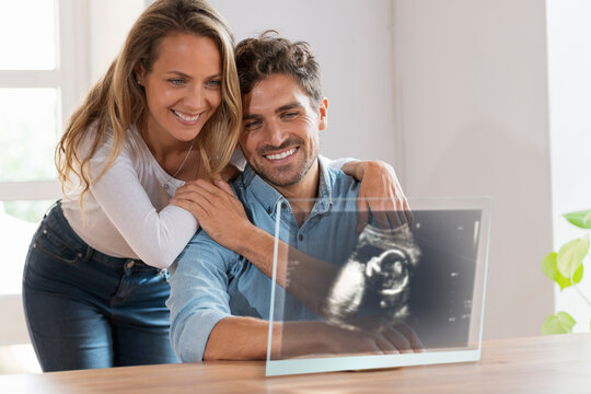 Affectionate couple looking at ultrasound image over transparent screen at home
