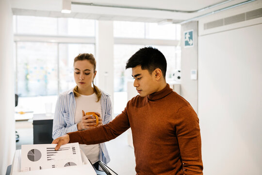 Businessman removing printout from by female colleague at office