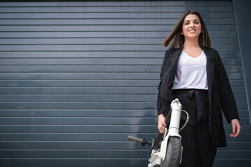 Businesswoman holding electric push scooter in front of shutter