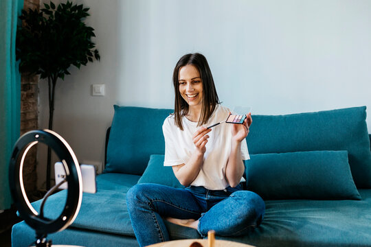 Smiling female influencer showing make-up palette during tutorial vlog