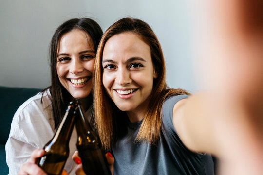 Happy young women taking selfie while toasting beer bottles