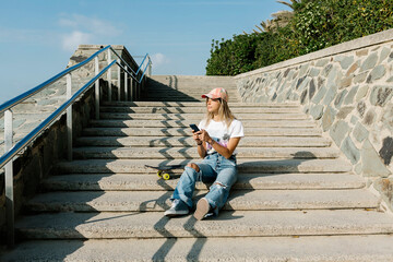 Mid adult woman with mobile phone contemplating while sitting on steps during sunny day