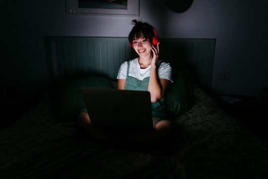 Smiling woman wearing headphones using laptop at home
