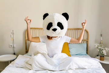 Woman wearing panda mask meditating on bed at home