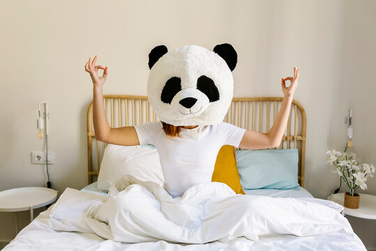 Woman wearing panda mask meditating on bed at home