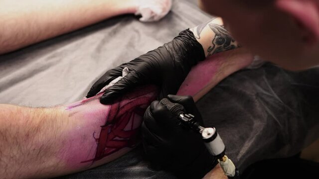 Tattoo salon - the client lying on the couch and getting a tattoo of big letters on his leg