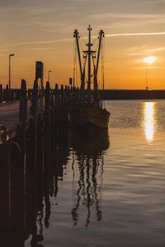 Denmark, Romo, Fishing boat moored to wooden pier at sunset