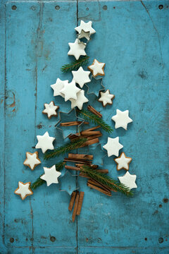 Christmas cinnamon star shaped cookies together with cinnamon and needle branches arranged in Christmas Tree on blue rustic wooden background