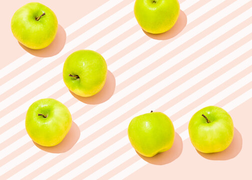 Studio shot of six green apples lying against pink striped background