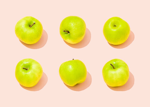 Studio shot of six green apples lying against light pink background