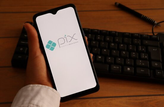 Bahia, Brazil - December 11, 2020. Woman's hand holding smartphone with Pix logo on screen, on office desk. Pix Brasil is an instant payment system.