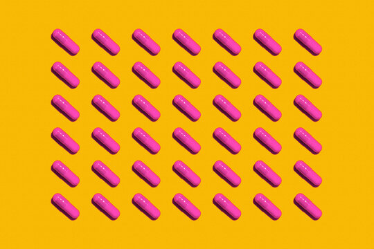 Pattern of rows of pink medicine capsules laid against yellow background