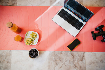 Laptop, smart phone, dumbbell and healthy breakfast on exercise mat at home