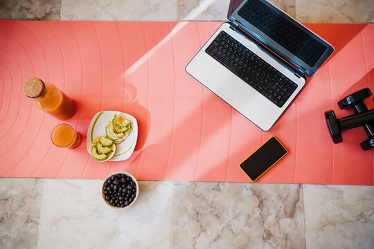Laptop, smart phone, dumbbell and healthy breakfast on exercise mat at home