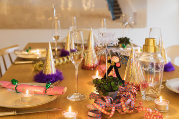 Festive laid New Years Eve table with plates, candles, party hats, champagne flutes and chimney sweep figurines