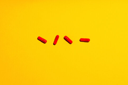 Four red medicine capsules laid against yellow background