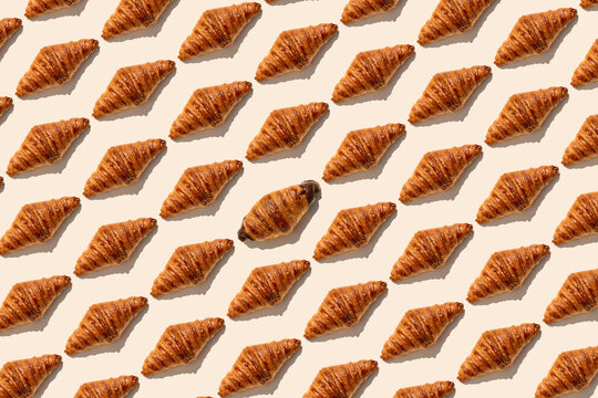 One chocolate croissant amidst butter croissants on beige background