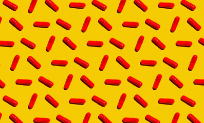 Pattern of rows of red medicine capsules laid against yellow background