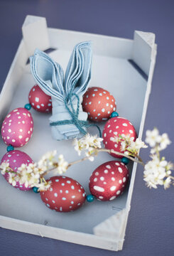 Blossoming twigs, napkin folded into shape of rabbit ears and wreath made of red spotted Easter eggs