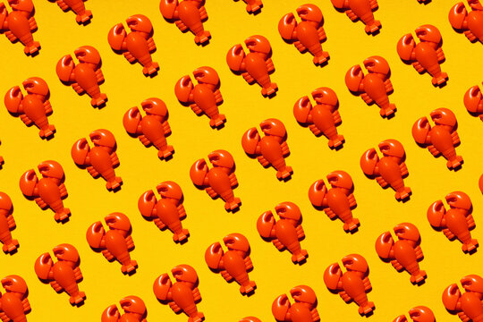 Pattern of rows of plastic lobsters flat laid against yellow background