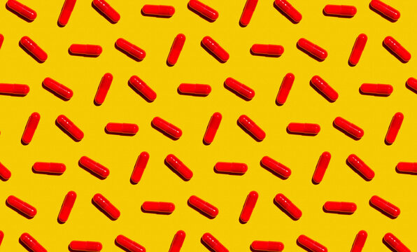 Pattern of rows of red medicine capsules laid against yellow background